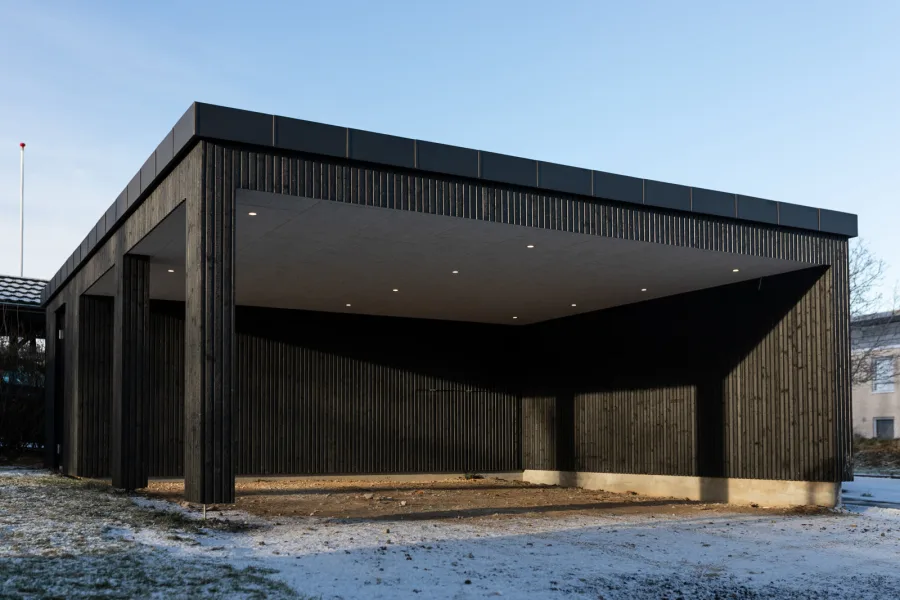 Carport / abri double neuf entièrement habillé d'un bardage bois vertical à claire-voie teinté noir, avec poteaux bois.