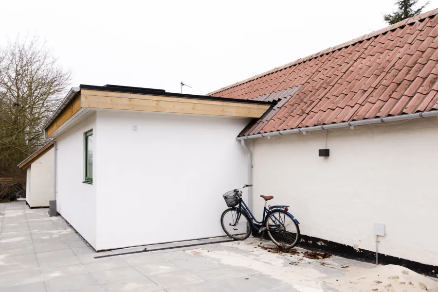 Extension à toit plat accolée à une maison ancienne : le toit-terrasse est fini par une étanchéité bitumineuse noire visible en rive avec bavette/couvertine, bandeau bois clair.